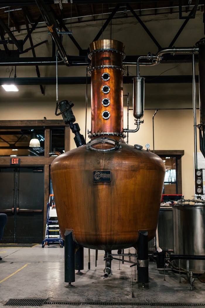 experience-img A copper distillation apparatus in an indoor industrial setting, showcasing brewery equipment.